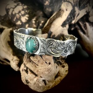 Intricately designed silver bracelet with a green stone centerpiece.